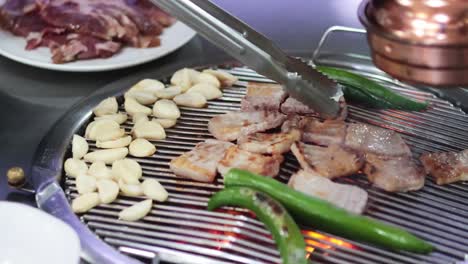 cooking meat, garlic, and peppers on a grill