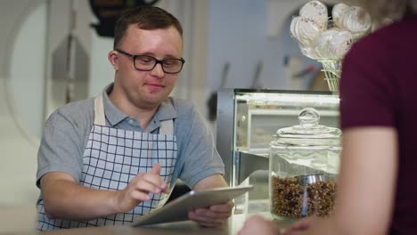 caucasian man with down syndrome taking order in the cafe using a digital tablet.