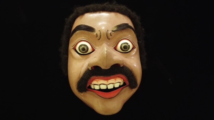 Maschera tradizionale in legno del teatro di danza Topeng di Bali Indonesia, primo piano su sfondo nero infinito.