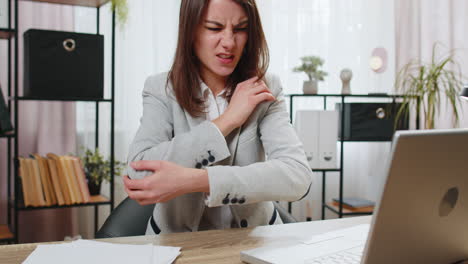 business woman sitting at home office experiencing pain and discomfort in elbow joint hand arthritis
