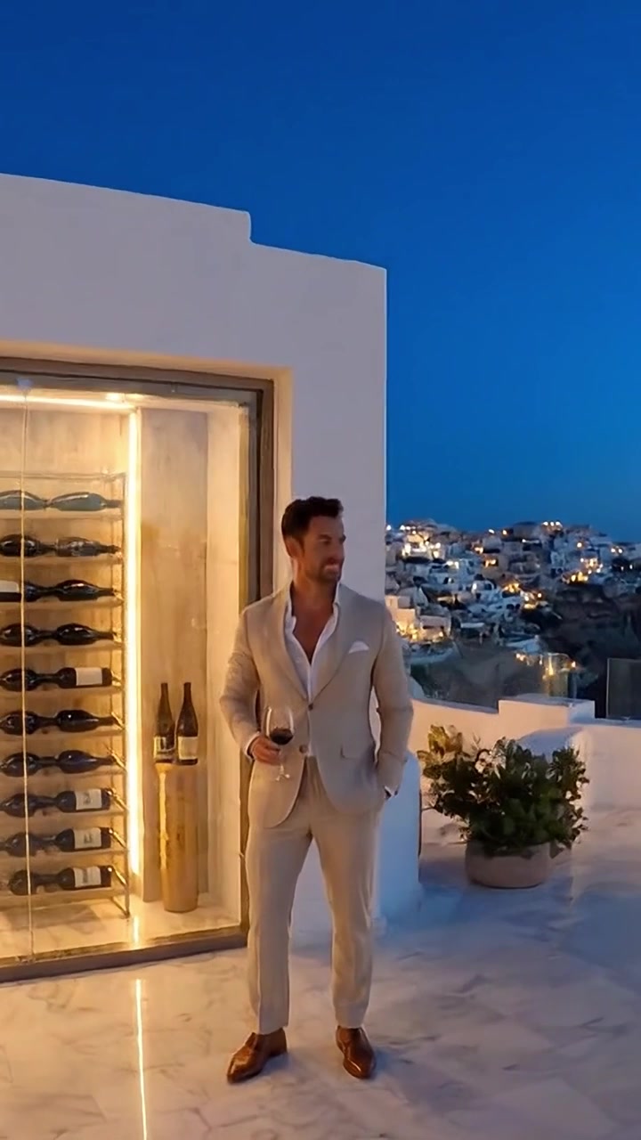 Una serata sofisticata su un rooftop con viste panoramiche di architettura bianca e luci scintillanti, accompagnata da un bicchiere di vino in mano.