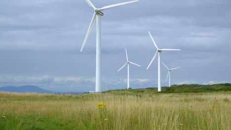aproximación de la turbina eólica a través de la hierba amarilla con cielo brillante nublado y horizonte nublado montañoso