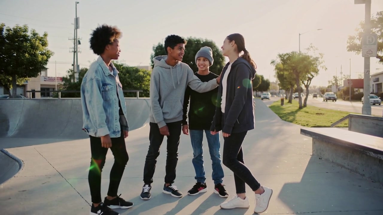 Forming circle four teens leaning placing hand on shoulder chatting at skate bowl with denim hoodie