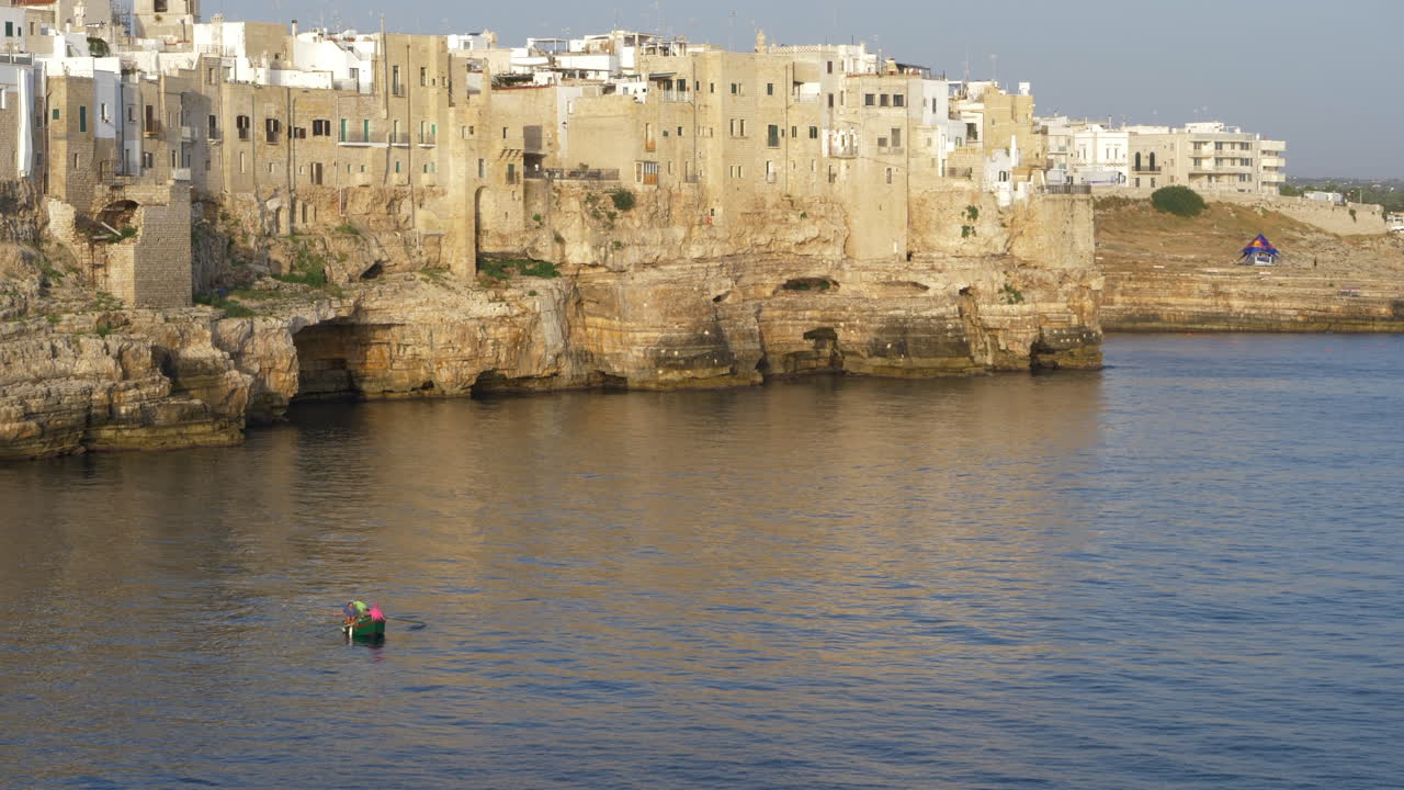 un barquero irreconocible navegando en la costa de polignano a mare, hora de oro