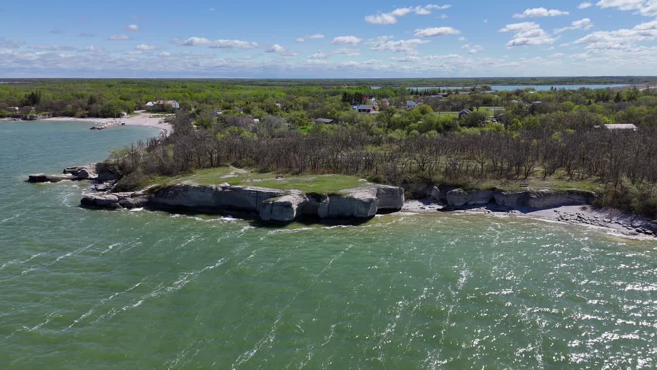 Dronový záběr ve Steep Rock v Manitobě, ukazující vápencové útesy, město, zelenou vodu jezera Manitoba, pobřeží a okolní stromy za slunného letního dne.