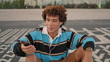 Smiling-zoomer-shooting-smartphone-street-closeup.-Guy-listening-music-vertical