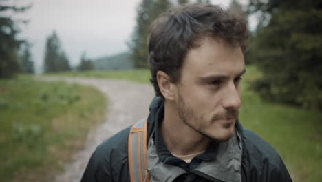 close up of a hiker walking on a road past the spruce trees looking around and admireing the nature, wearing windproof jacket and a backpack