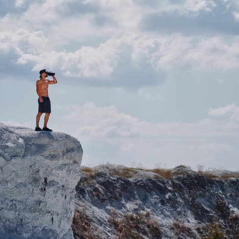 athlete drinking water on a white rock in summer. shirtless man with flask in white canyon in a sunny day. healthy sportsman after training outdoors.