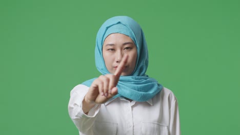 close up of asian muslim woman disapproving with no index finger sign while standing in the green screen background studio