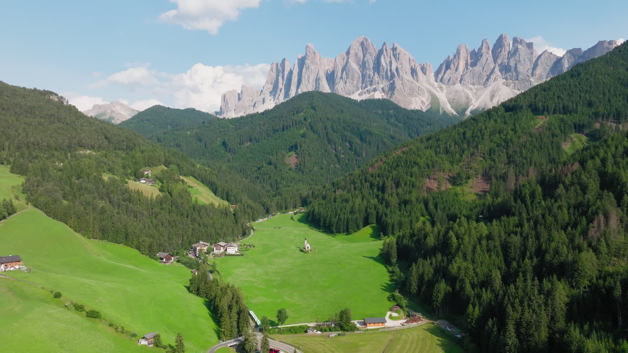 Church of St. John in lush green Dolomite valley framed by distant peaks and forest