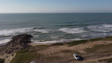 Two-friends-standing-and-looking-waves-of-Atlantic-ocean,-Chapadmalal-beach-at-Mar-del-Plata-in-Argentina