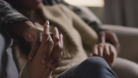 Close-Up-Of-Loving-Couple-Holding-Hands-Relaxing-At-Home-Sitting-On-Sofa-Talking-Together