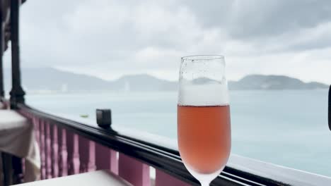 a kir royal cocktail sits on a balcony overlooking a rainy seascape in phuket, thailand, capturing a serene and moody atmosphere