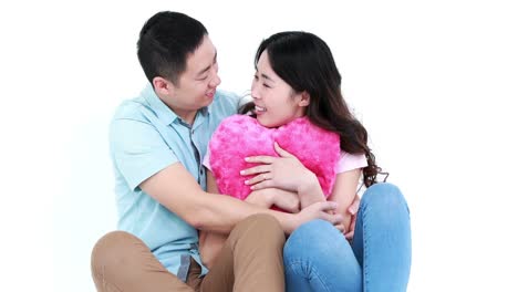 Smiling-Asian-couple-sit-together-and-hugging-a-pillow