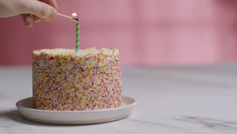 single candle being lit by hand on studio shot of birthday cake covered with decorations