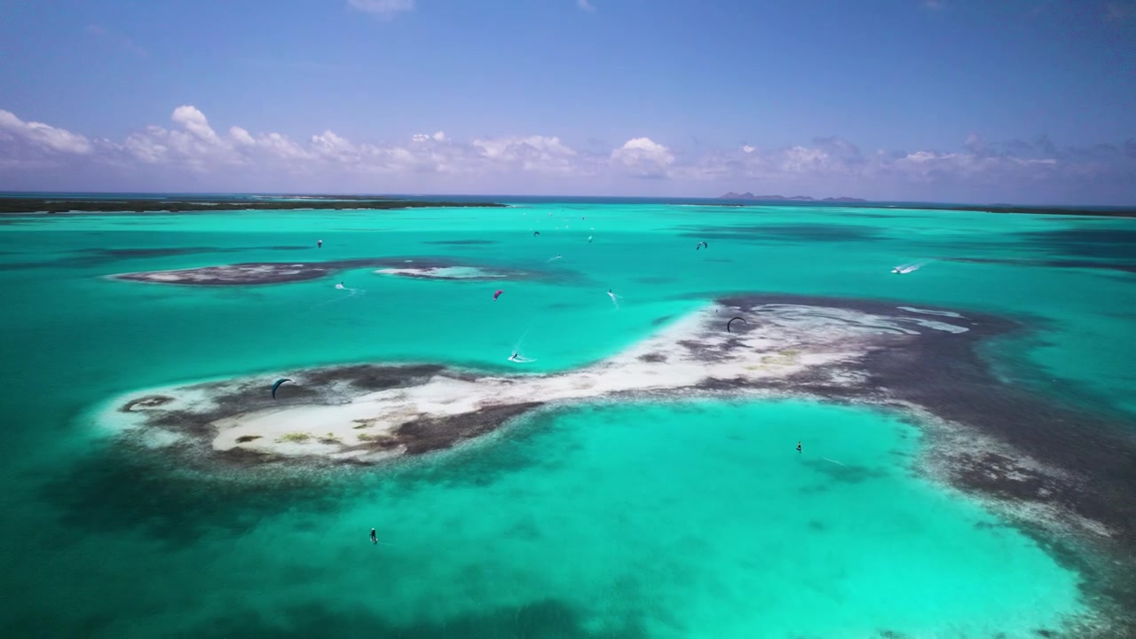 Kitesurfer che planano su acque turchesi a Los Roques sotto un cielo sereno, vista aerea.