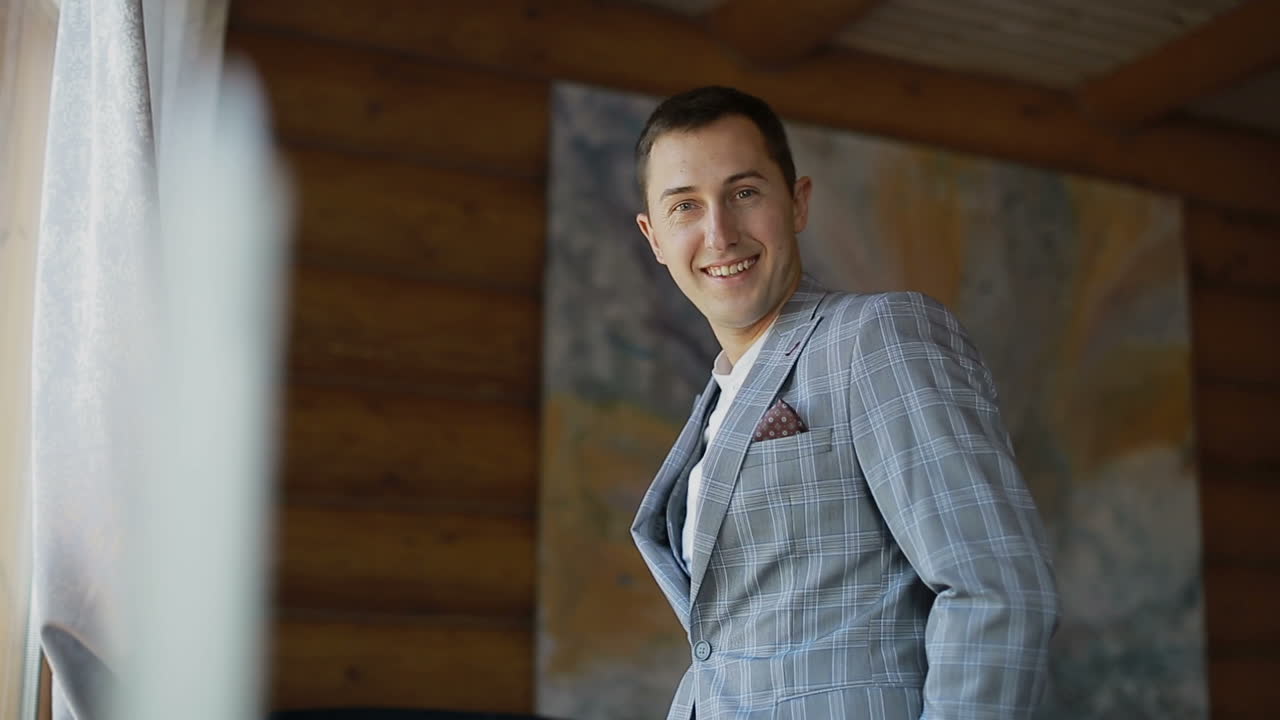 Young handsome man is wearing a jacket, standing in front of a window. Men's Clothing.