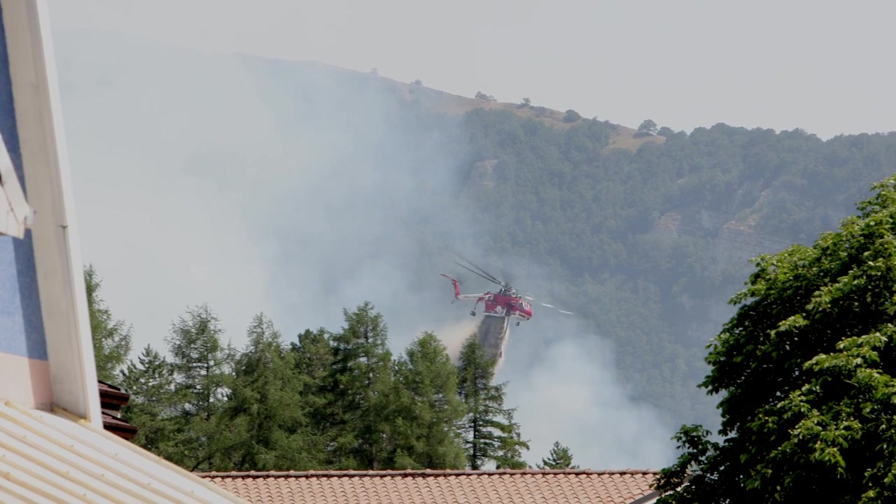 A Sikorsky S-64 Skycrane helicopter dropping water on a forest fire developing near a town. Rocca di Mezzo, Abruzzo region. Italy. Summer 2026