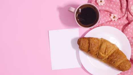 romantic arrangement with fresh croissant and cup of coffee next to paper card note. stop motion