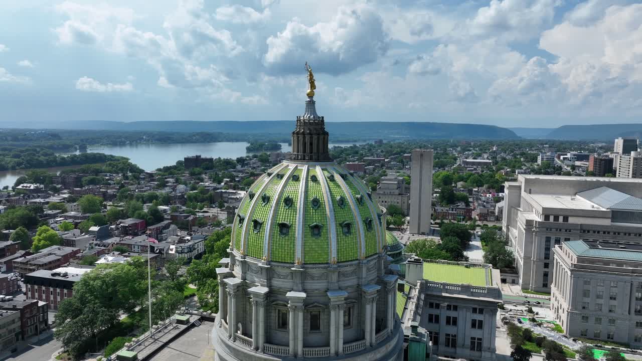 Aerial orbit of green cupola of Pennsylvania state capitol building in Harrisburg. Sunny day with clouds at sky. Historic buildings in American town