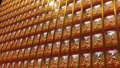 Wall-of-amber-Buddha-statues-behind-glass-in-Longhua-Temple-in-Shanghai,-China-in-dynamic-motion