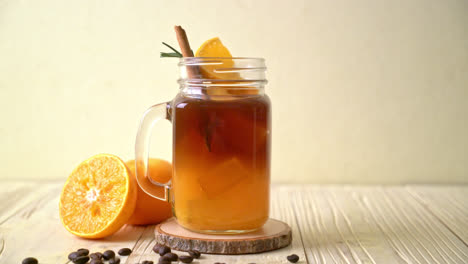 un vaso de café negro americano helado y una capa de jugo de naranja y limón decorado con romero y canela