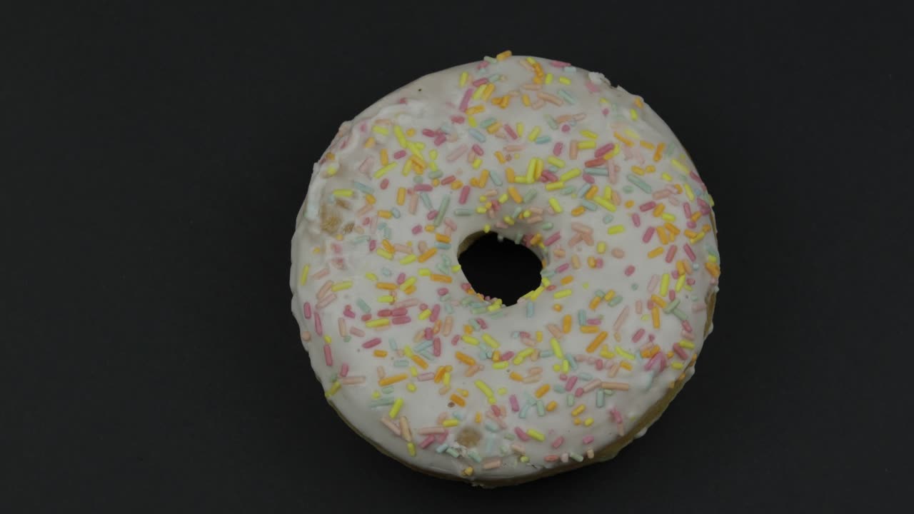 donut dulce girando sobre un fondo negro. vista superior. donut sabroso y fresco rociado