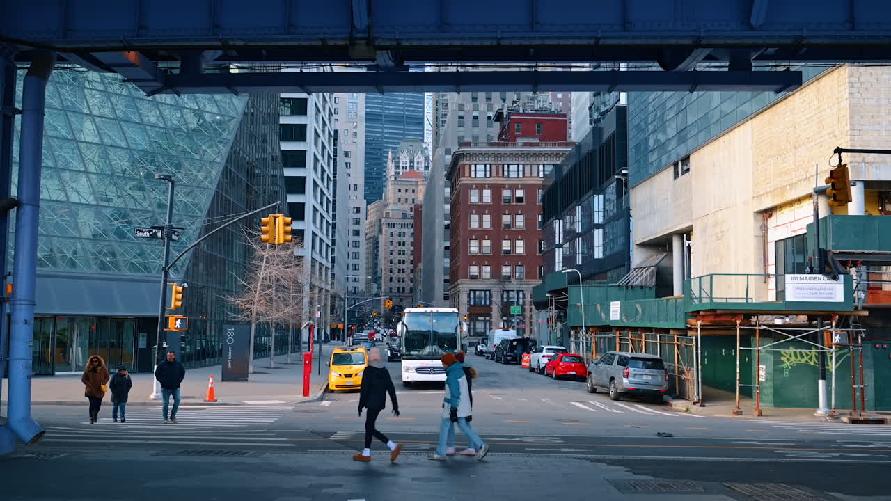 New York, USA, 18 dicembre 2025: Passeggiata per strada sotto il viadotto. Persone attraversano la strada all'incrocio. Edifici di New York sullo sfondo.