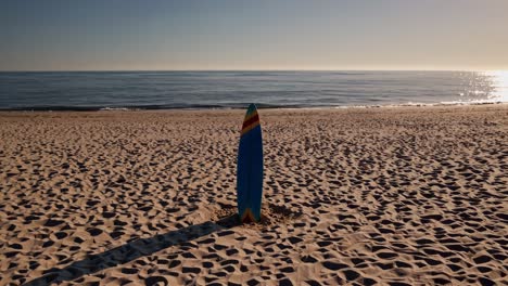 colorful surfboard stands upright on a sandy beach, the morning sun reflecting off the calm ocean in the background, creating a serene and peaceful scene