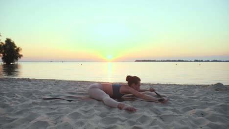 estiramiento al aire libre. banda elástica de fitness. mujer joven atlética está haciendo ejercicios usando banda elástica de fitness, en la playa durante la puesta o el amanecer. entrenamiento de fitness al aire abierto. hacer deportes por la mañana. fitness, deporte, yoga y estilo de vida saludable