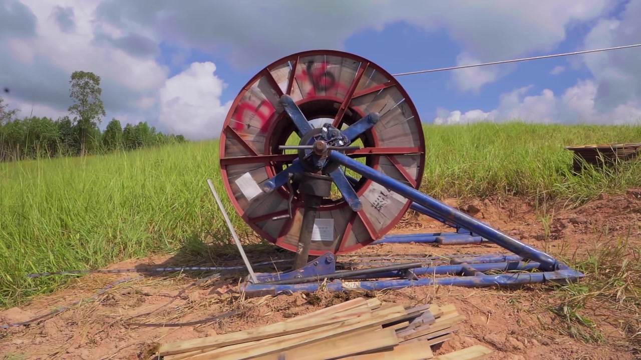 Large industrial reel unwinding fiber optic cable for communication infrastructure in a rural field in Minas Gerais, Brazil. Slow motion concept