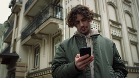 focused man texting on smartphone outdoor. positive hipster holding cellphone.