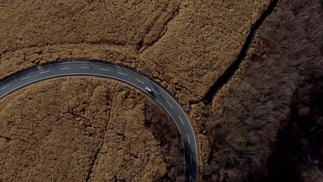 a curvy road cutting through a brown, textured landscape, possibly autumn, aerial view