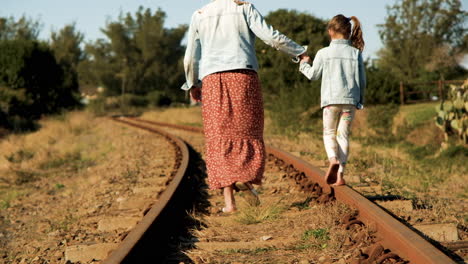 Mom-gives-helping-hand-to-daughter-balancing-on-train-tracks-as-they-walk