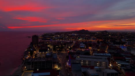 aerial ascend of punda and pietermaai districts in curacao at sunset, colorful buildings with a vibrant pink sky at dusk, building lights illuminated