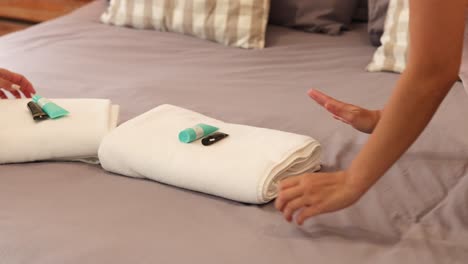 hands folding towels on a bed with toiletries, in a softly lit hotel room