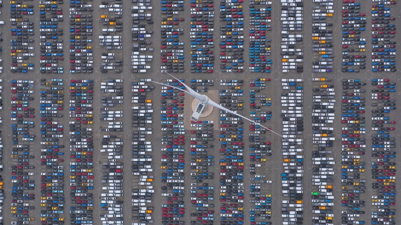 Aerial view of export cars parked near spinning wind turbine, trade hub