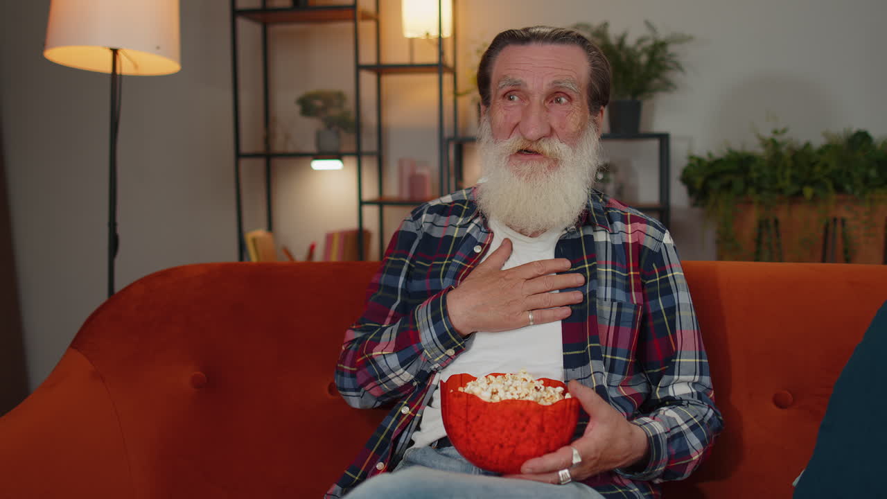Evde koltukta oturmuş patlamış mısır yiyen ve ilgi çekici bir TV dizisi veya spor maçı izleyen adam