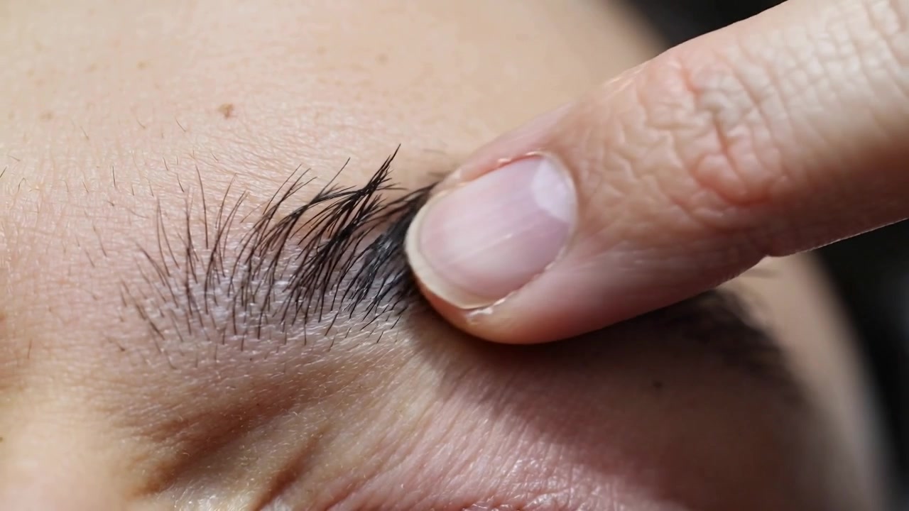 Pressing inner brow, fingertip brushing eyebrow hairs in studio, aligning skin for grooming