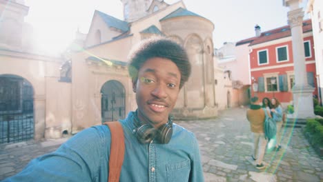 african american man holding smartphone and talking to the camera while pointing to his friends behind