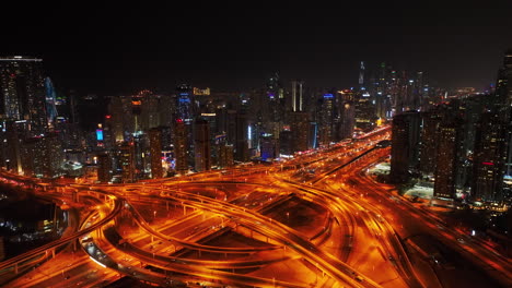 aerial descending footage of vehicles passing through large highway interchange in night city