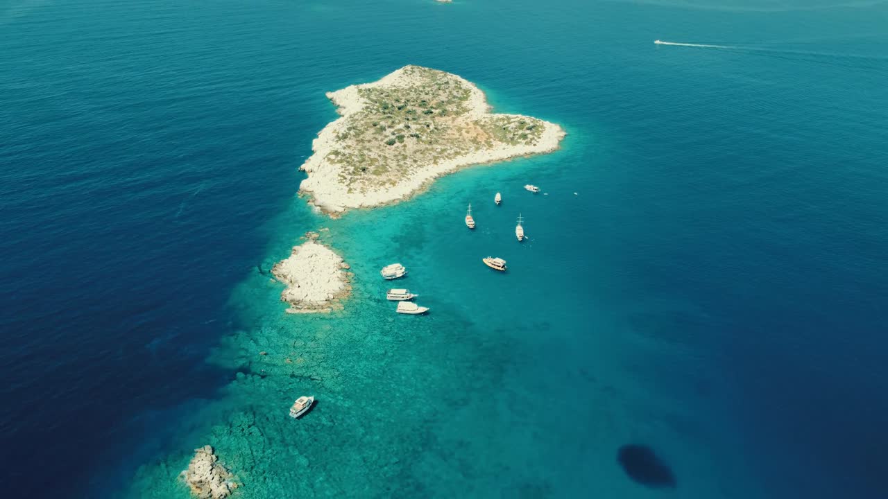 Aerial drone view showing heart shaped island with anchored boats near Gocek Bay in Mugla, capturing clear turquoise water, rocky coastline, calm sea surface, and bright summer atmosphere
