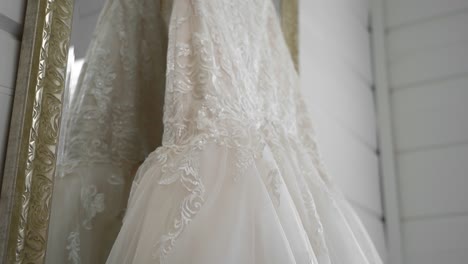 Revealing-the-details-of-a-elegant-white-wedding-gown-hanging-from-a-gold-framed-full-length-mirror-in-a-well-lit-and-clean-white-room-at-Le-Belvédère-in-Wakefield,-Quebec,-Canada