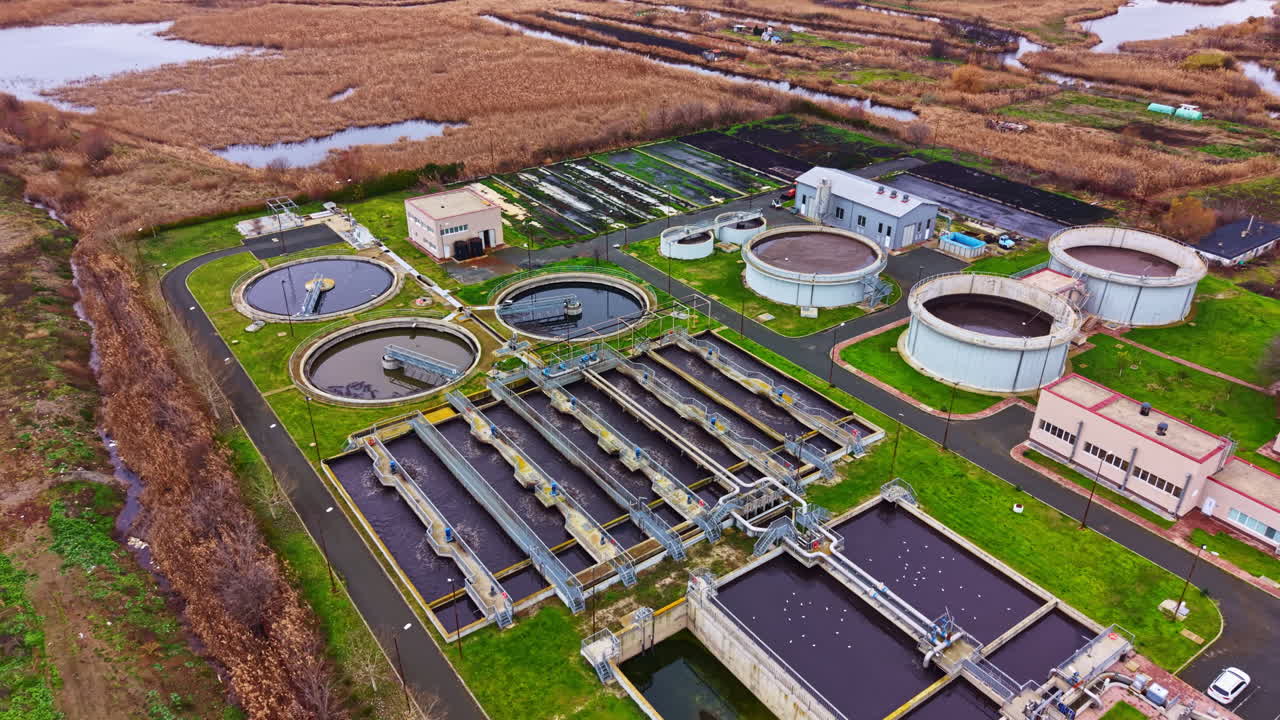Water treatment facility located in a rural area with various tanks and buildings engaged in processing water in daytime surrounded by wetland vegetation