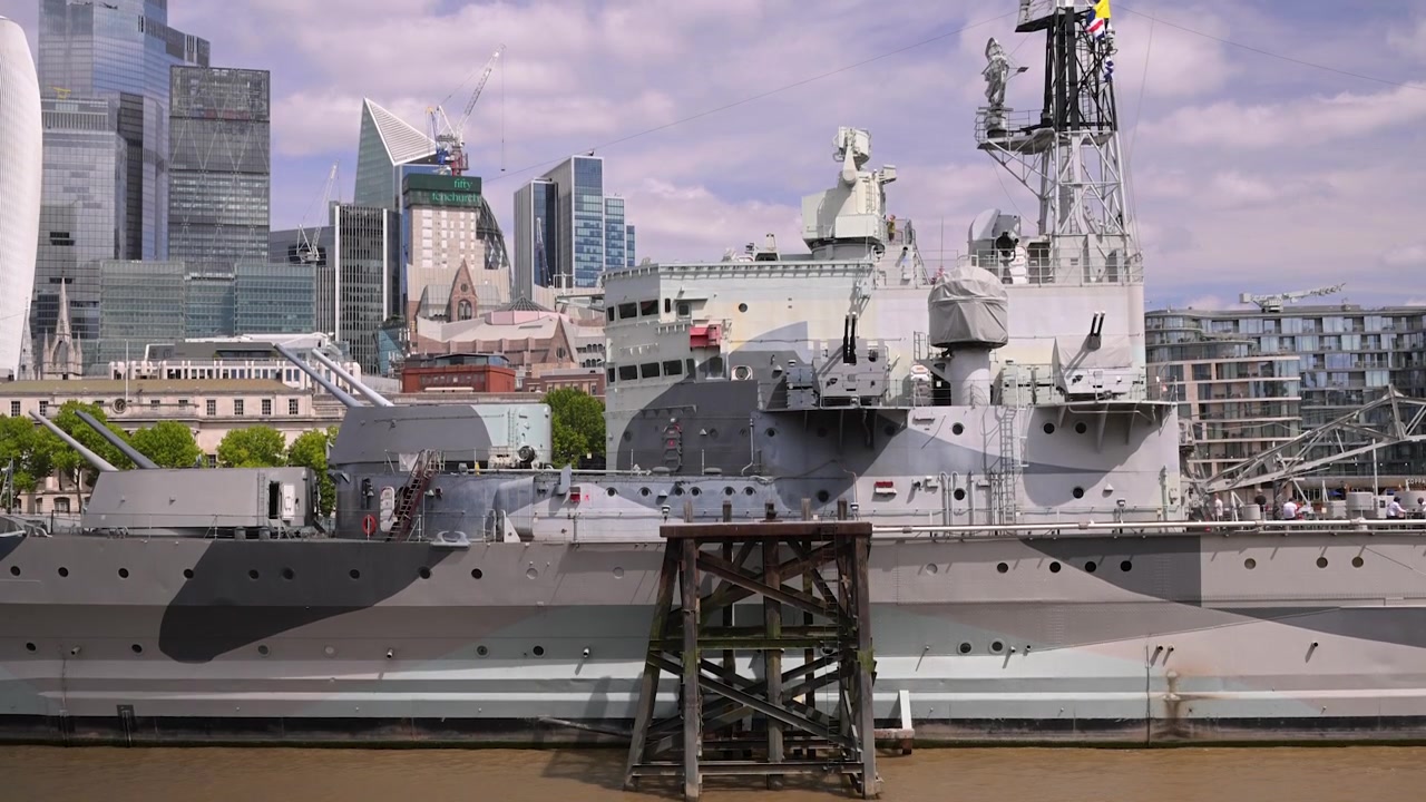 Museumoorlogsschip HMS Belfast ligt afgemeerd aan de Theems met moderne wolkenkrabbers van de City of London op de achtergrond op een heldere dag