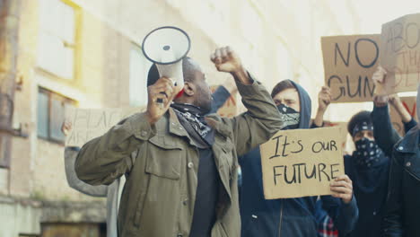 African american man with arms up yelling on a loudspeaker in a protest with multiethnic group of people in the street