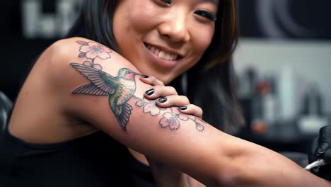 a close-up journey of a tattoo artist capturing the beauty of a colorful hummingbird nested among delicate cherry blossoms on an enthusiastic client's arm