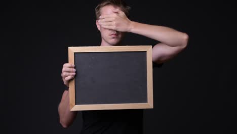 man holding empty blackboard while covering his eyes