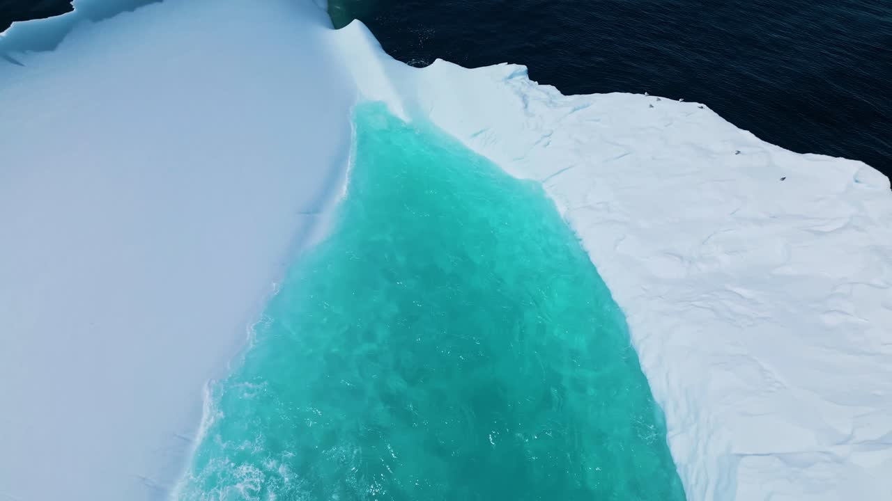 Aerial footage of a large iceberg off Flatrock, Newfoundland, featuring vivid turquoise meltwater in calm Atlantic waters.
