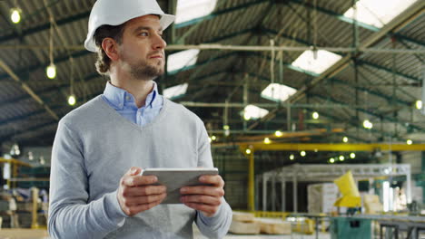 caucasian male worker wearing a helmet using a tablet and looking around in a factory